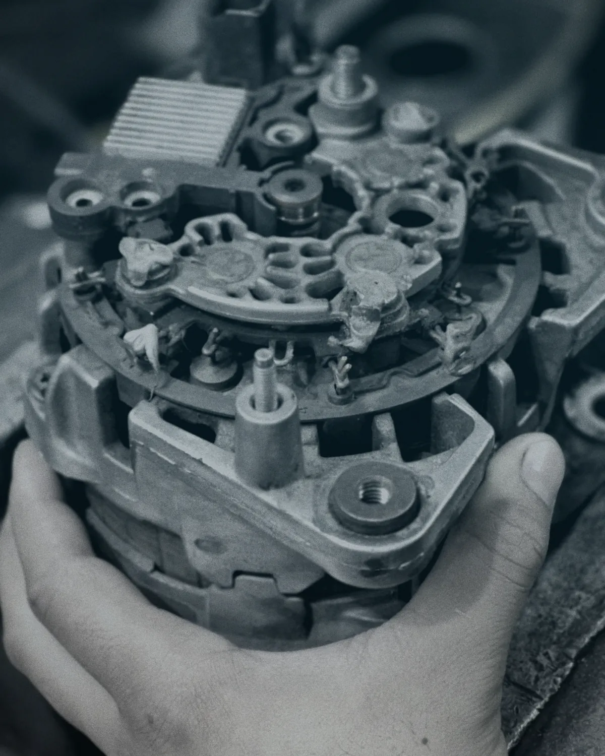 Alternador desarmado en la mano del técnico durante su reparación
